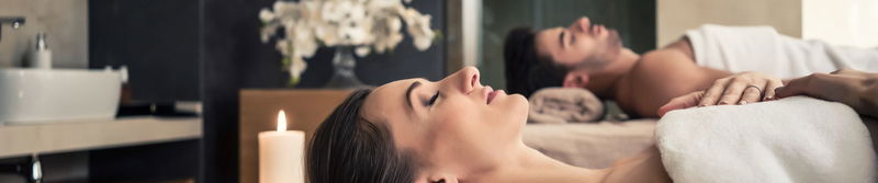 Paar nebeneinander bei einer Massage im Spa, daneben Kerze und Orchidee