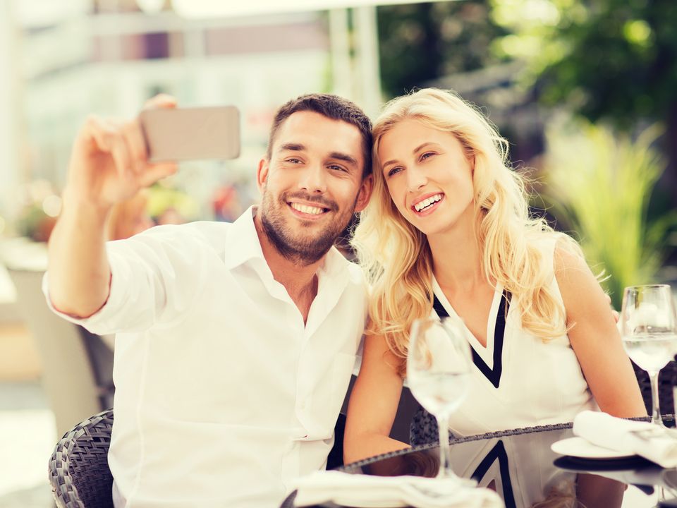 Lächelndes Paar macht ein Selfie am Tisch eines Straßencafés