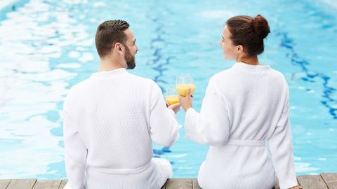 Paar sitzt im Bademantel mit Getränken am Pool