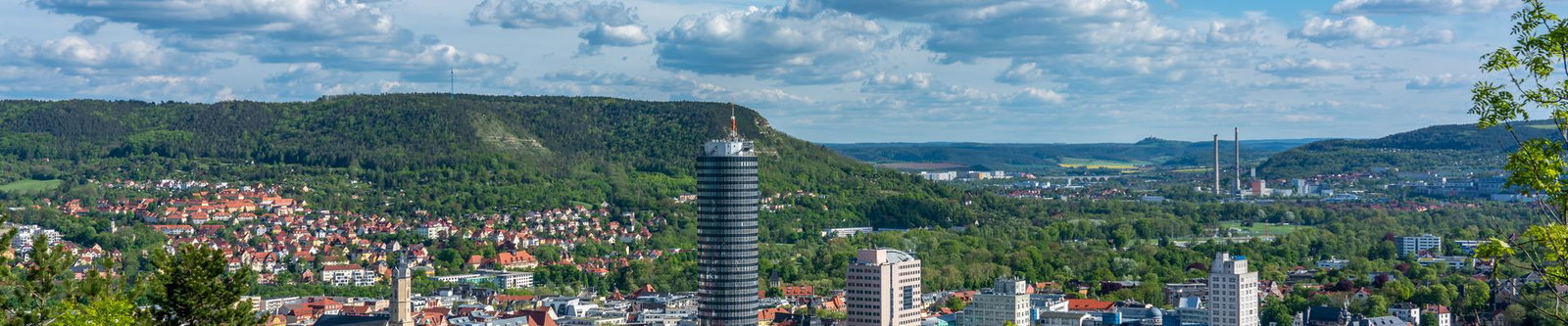 Blick über Jena im Saaletal mit dem runden Hochhaus vor bewaldeten Hängen