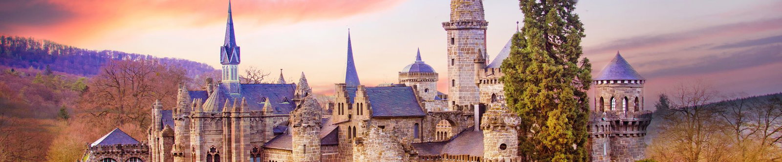 Neugotische Löwenburg mit Türmen und Zinnen über bewaldeten Hügeln im rosafarbenen Abendlicht