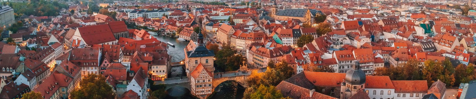 Altes Rathaus auf seiner Brücke über der Regnitz zwischen den roten Ziegeldächern der Bamberger Altstadt im Abendlicht