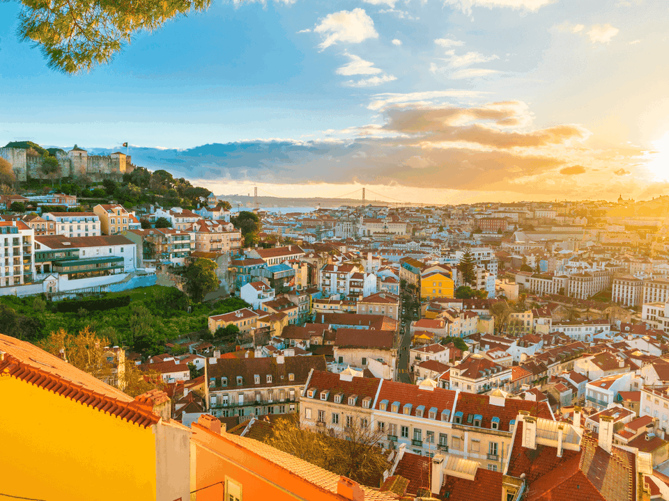 Blick über die roten Ziegeldächer einer Altstadt mit Burg und Fluss im Sonnenuntergang