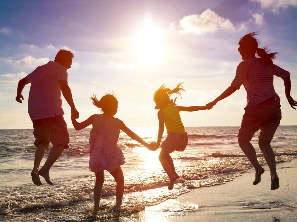 Familie mit zwei Kindern springt Hand in Hand durch die Brandung im Sonnenuntergang