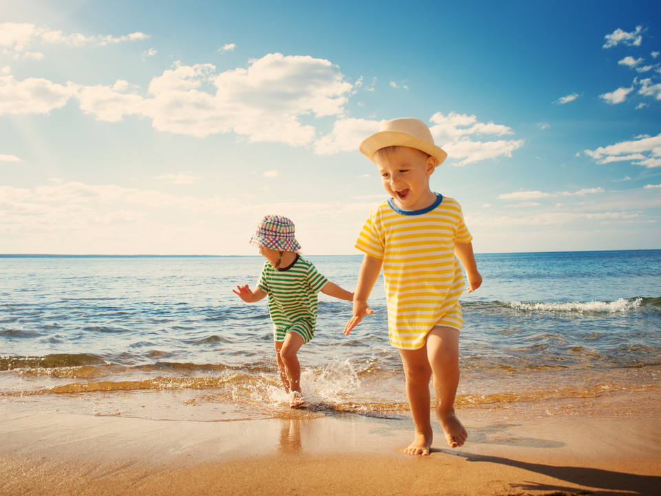 Zwei Kinder laufen lachend durch die Brandung am Strand