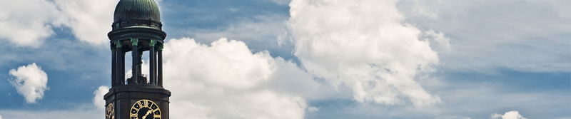Kirchturm mit Turmuhr und grüner Kuppel vor Wolkenhimmel