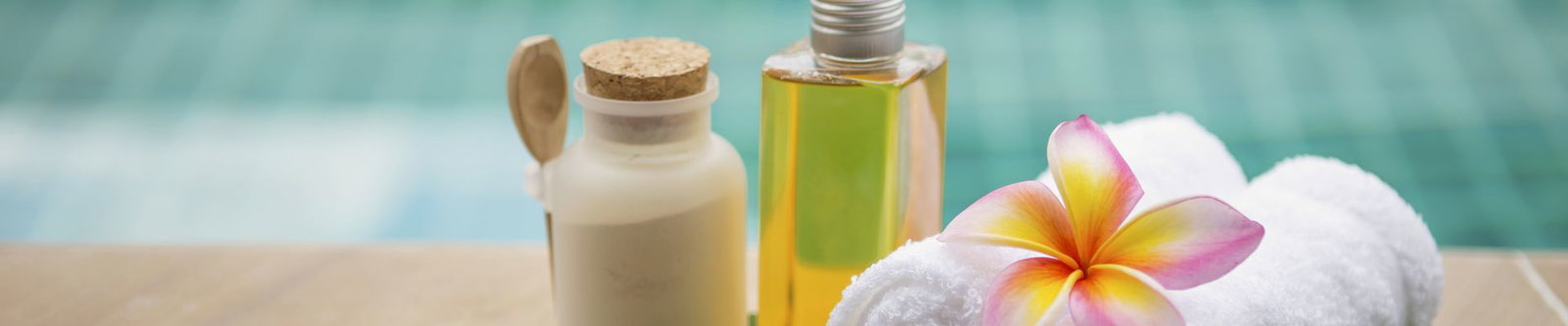 Badesalz, Massageöl und Handtuch mit Frangipani-Blüte am Rand eines Pools
