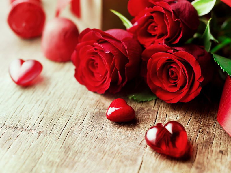 Rote Rosen und kleine rote Herzen auf rustikalem Holz