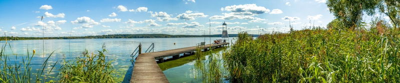 Holzsteg mit Leuchtturm im Schilf an einem weiten See