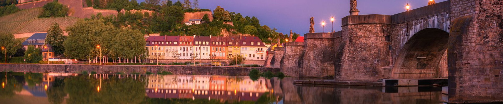 Alte Mainbrücke und Häuserzeile am Ufer unterhalb der Weinberge in der Abenddämmerung