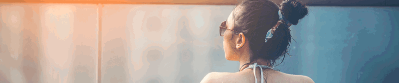 Frau mit Sonnenbrille und Haarknoten von hinten im Abendlicht
