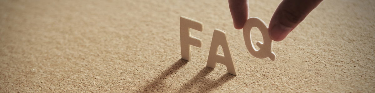 Eine Hand stellt den Buchstaben Q zu den bereits stehenden Holzbuchstaben F und A auf einer Oberfläche, sodass das Wort FAQ entsteht.