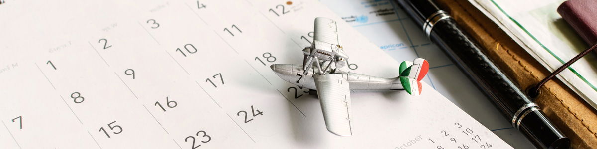 Ein Modellflugzeug liegt auf einem aufgeschlagenen Kalender neben Stift und Notizbuch und symbolisiert Reiseplanung, Urlaubsbuchung oder Terminplanung für eine Reise.