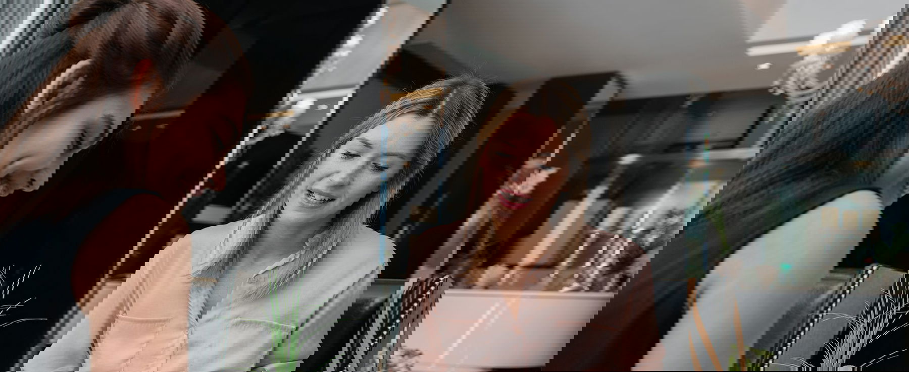 Zwei Frauen sitzen an einem Tisch in einem modernen Innenraum und unterhalten sich freundlich, während sie gemeinsam Unterlagen ansehen.